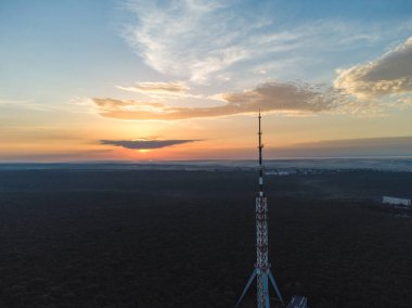 Telekomünikasyon kulesi antenli ve şafak vakti bulutlu gökyüzü manzaralı havadan yaz manzaralı bir orman. Kharkiv, Ukrayna