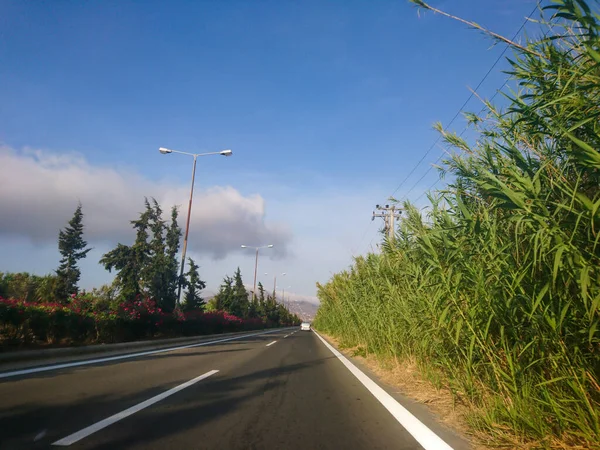 ギリシャ ヨーロッパの歩道上の葦や花とアウトバーンアスファルトの道路を運転 テッサロニキからアテネへの旅行 自動車からの景色の良い雲 — ストック写真