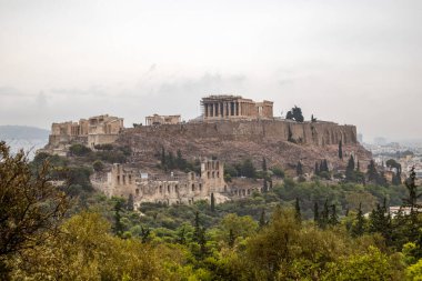 Akropol Tepesi (Parthenon, Propylaea, Tapınaklar, Kahraman Atticus Odeonu) yaz yeşilliğinde. Bulutlu bir günde Atina Filopappou Tepesi 'nden kent merkezindeki tarihi eser