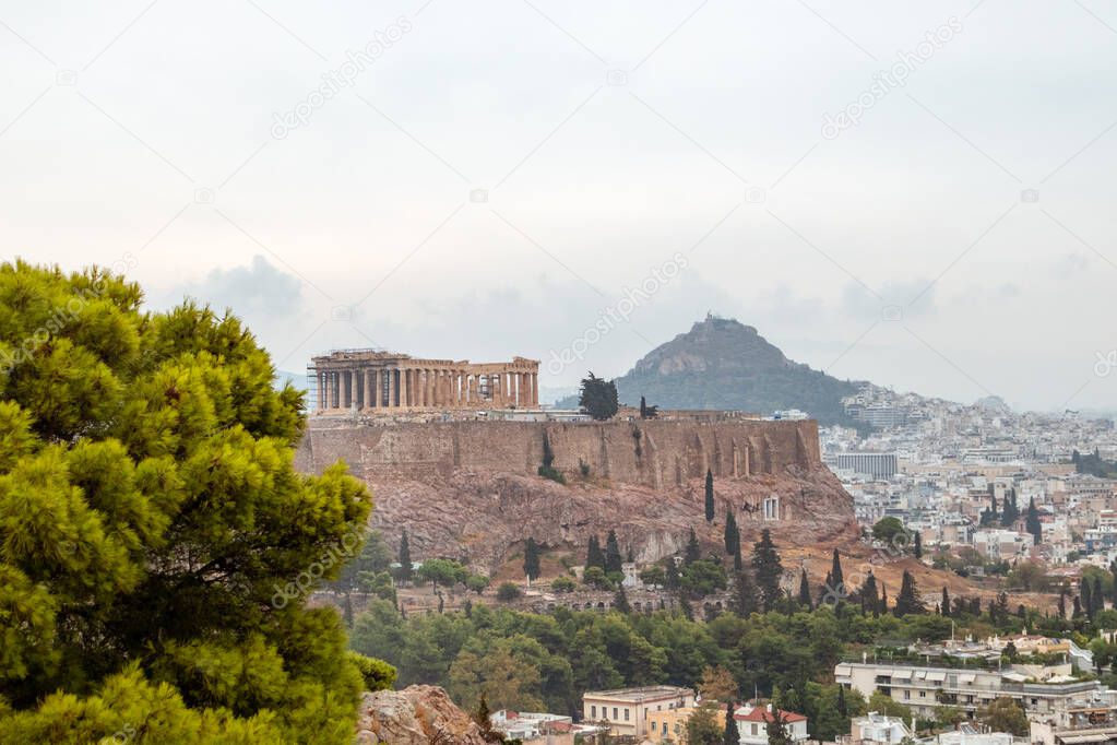 Acropolis (Parthenon, Temples), Mount Lycabettus and white city buildings with vivid pine summer greenery. Athens ancient historical landmark from Filopappou Hill on cloudy day