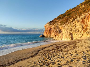 Yunanistan 'ın Lefkada adasının kıyılarında, parlak günbatımı ışığında gök mavisi renkli dalgalarla dolu Mylos kumlu plajı. İyon Denizi 'ne yaz tatili