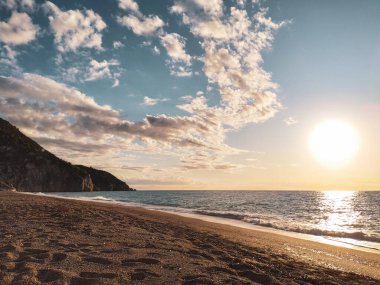 Yunanistan 'ın Lefkada adasında, Mylos kumlu sahilinde güneş batarken, gök mavisi dalgalar esiyor. İyon Denizi 'ne yaz tatili