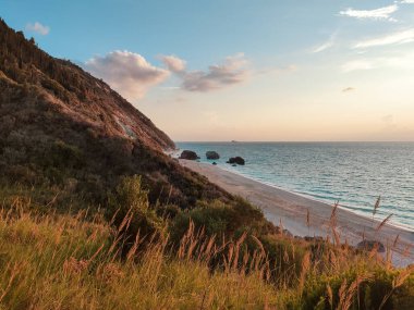 Plaj Megali Petra gün batımı manzaralı. Yeşillik, tepeler ve gün batımında çakıl taşları olan dalgalar. Lefkada adasının Yunanistan 'da sarp kayalıkları olan kıyıları. İyon Denizi 'ne yaz tatili