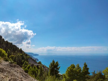 Yunanistan 'da açık mavi bir günde güneşli deniz kıyısındaki yeşil uçurumlar. Turkuaz su ve açık mavi gökyüzü, Lefkada adası, İyon deniz kıyısı.