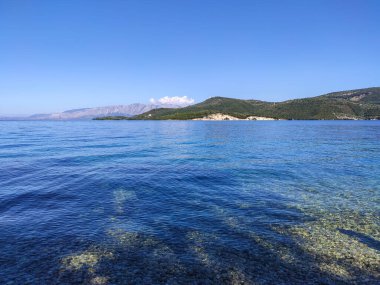 Mavi berrak, durgun İyon Denizi suyu, açık gökyüzü ve yeşil tepeler. Yunanistan 'daki Lefkada adasının doğası. Yaz tatili için cennet gibi bir tatil yeri.