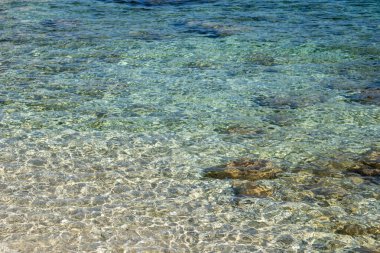 Yunanistan 'ın Lefkada adasının kıyısındaki çakıl taşı plajında açık deniz yüzeyi manzaralı yakın çekim döngüsü. Güneş masmavi sularda parlıyor.