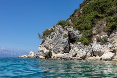 Yeşil kayalıkları ve parlak gökyüzü olan İyon Denizi 'nin mavi sularındaki manzara kayaları. Yunanistan 'daki ada doğası. Yaz tatilinde gidilecek yer