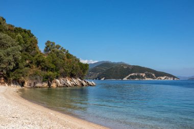 Pebble Kamari Sahili manzaralı kayalar, mavi berrak durgun İyon Denizi suyu, canlı gökyüzü ve uzak yeşil tepeler. Yunanistan 'daki Lefkada adasının panoramik manzarası