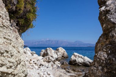 Yunanistan 'ın Lefkada adasının çakıl taşları sahilinde Akdeniz yeşili ve açık mavi gökyüzü olan beyaz büyük kayalar. Yazın İyon Denizi 'ne vahşi doğa yolculuğu