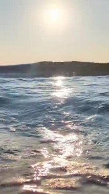 Gün ışığında kumsalda hafif deniz dalgaları berrak gökyüzünün altında su yüzeyinde parıldayan yansımalarla