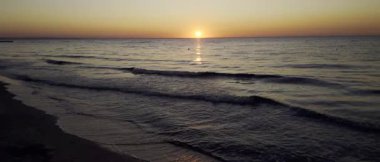 Gün doğumunun sinematik yavaş çekim görüntüsü sakin deniz yüzeyine altın dalgalar ve yumuşak hareketlerle yansıyor