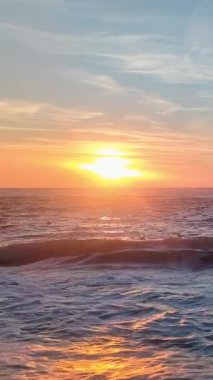 Dikey parlak gün doğumu ufukta parlayan güneş ve kumlu sahil dalgaları