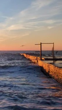 Dalgalar denizdeki eski beton iskeleye vuruyor altın gibi parlak sabah ışığında