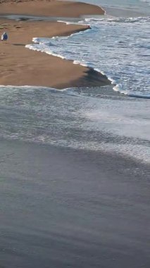 Güneşli, dikey deniz dalgalarının altın kumda yuvarlanan köpüklü görüntüsü.