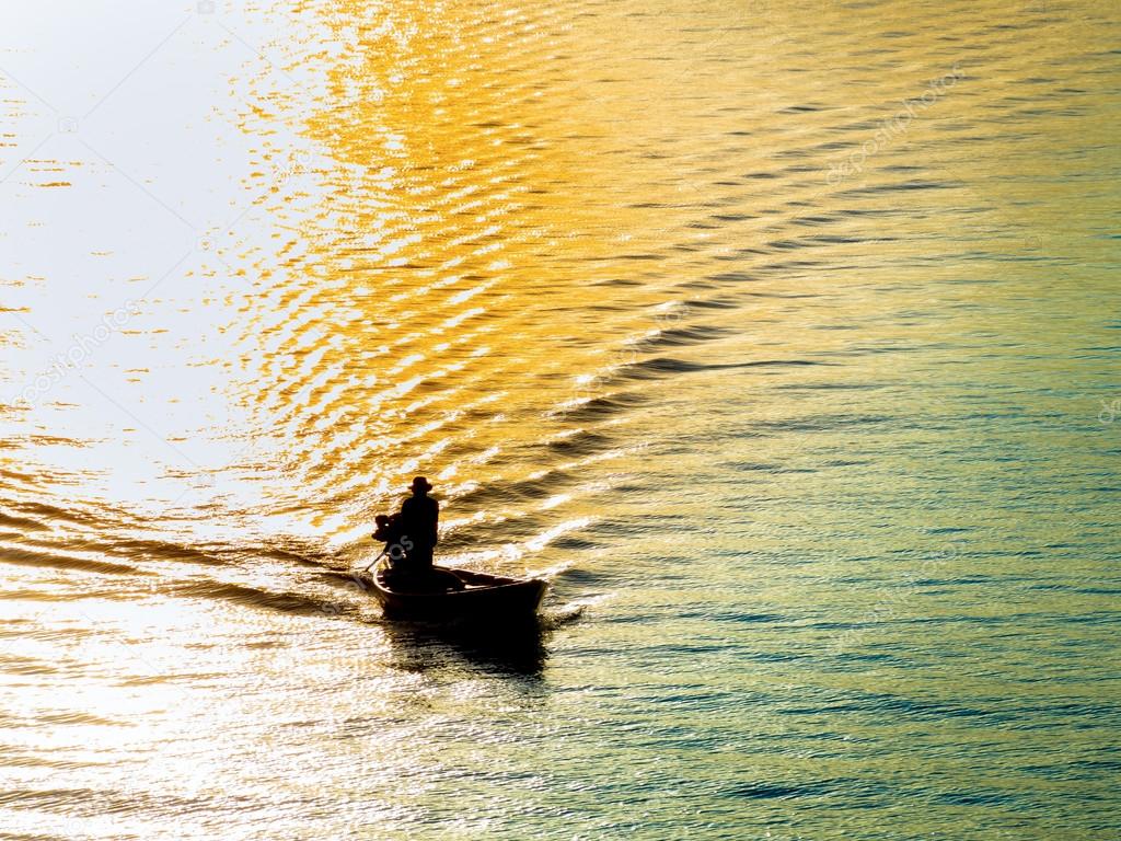 silhouette of fisherman on a boat passing through the sunrise
