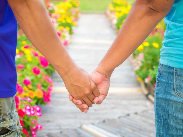 Close-up em segurar as mãos do casal homem e mulher na flor — Fotografia de Stock