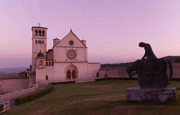 La statua di San Francesco con la Basilica di Assisi sullo sfondo al tramonto — Foto Stock