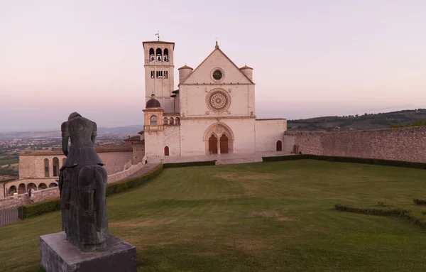 La estatua de San Francisco con la Basílica de Asís al fondo al atardecer — Foto de Stock