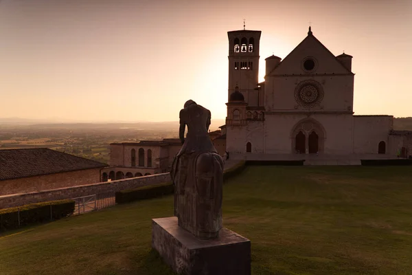 Het standbeeld van Sint Franciscus met de Basiliek van Assisi op de achtergrond bij zonsondergang — Stockfoto