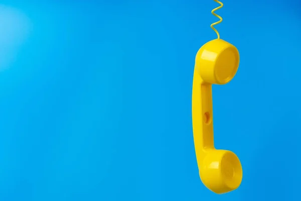 Mavi arkaplanda sarı retro telefon alıcısı.