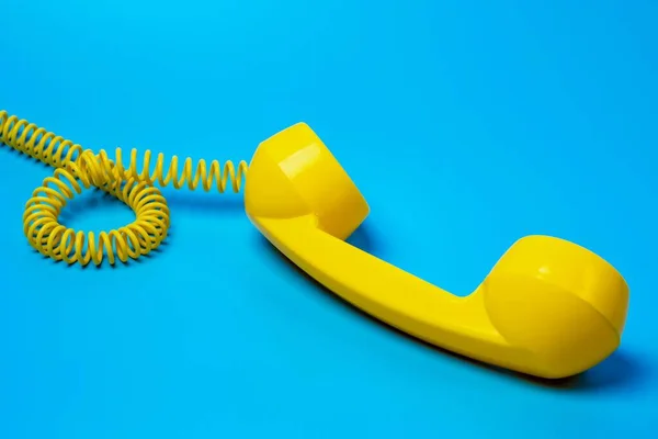 Mavi arkaplanda sarı retro telefon alıcısı.