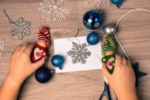 Noel arkaplanı bir çocuğun elleriyle ahşap bir masada yeni yıl süslemeleri hazırlıyor. Yukarıdan bak. Yeni yıl tatiline hazırlanma konsepti.
