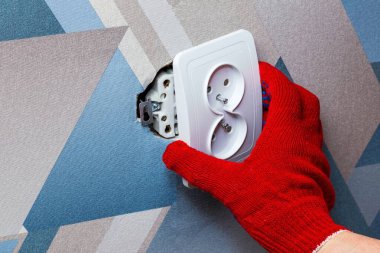 Kırmızı koruyucu eldiven giyen bir elektrikçi oturma odasının duvarına soket takmak için tornavida kullanır. Elleri yakın çekim. Ev sahibi kavramı.
