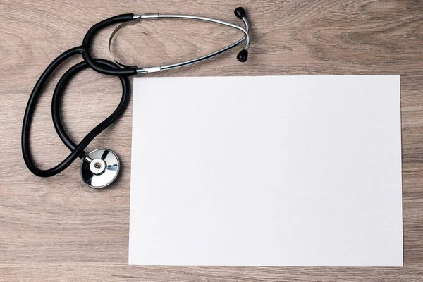 A medical stethoscope and a white sheet of paper lie on the textured wood surface of the table. Copy space