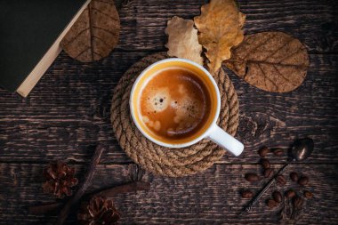 Halat altlığında bir fincan kahve, bir kitap, meşe yaprakları, bir kaşık ve kahve çekirdeği eski kahverengi ahşap bir masanın üzerinde. Düz yatıyordu