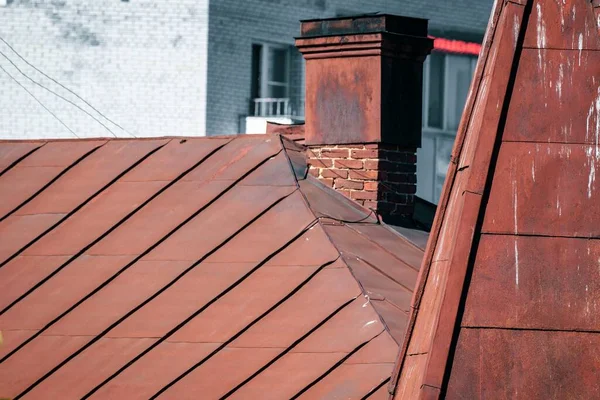 Blick auf das rostige Metalldach eines alten Hauses mit gemauertem Schornstein. — Stockfoto