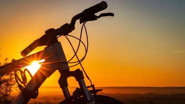 Silhueta de uma bicicleta contra o pano de fundo de um pôr do sol com belos raios do sol. — Fotografia de Stock