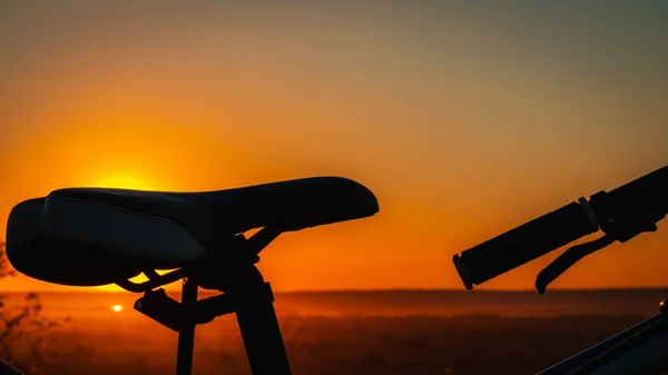 Silhueta de uma bicicleta contra o fundo de um pôr-do-sol com um céu laranja. — Fotografia de Stock