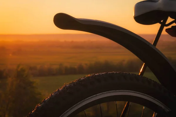 Silhueta de uma bicicleta contra o fundo de um pôr-do-sol com um céu laranja. — Fotografia de Stock