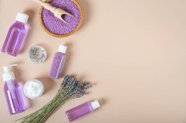 Lavanta suyu. Şeffaf şişelerde lavanta özü ve lavanta çiçekleri. Bej arka planda lavantalı kozmetik seti