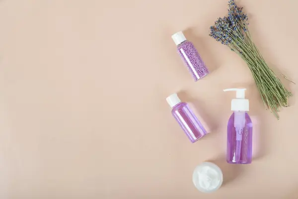 beauty product samples from lavender flower on white wooden table background, soft light. set of cosmetics with lavender, face cream and lavender shampoo.