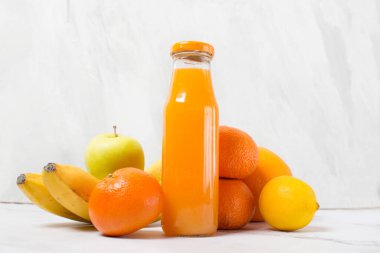 Arka planda yaprakları ve meyveleri olan meyve suyu bardakları. Cam şişede taze narenciye suyu, mandalina suyu, gri arka planda elma ve limon.