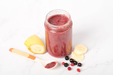 Kavanozda muzlu bebek böğürtlen püresi. Doğal bebek maması konsepti: taze eriklerin yanındaki masada erik aromalı elma püresi kavanozu