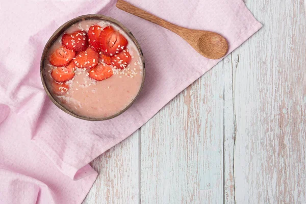 strawberry smoothie in a coconut bowl. Smoothie bowl with chia seeds, muesli, strawberries, banana slices and coconut flakes