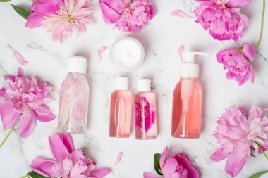 Kozmetik ürünler. Beyaz mermer arka planda esaslı yağlar, güzel şakayıklar. Düz yerde, üst tarafta. Yüz bakımı için masaj yağları, güzellik kaplıcası konsepti