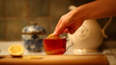 woman putting fresh lemon into black tea