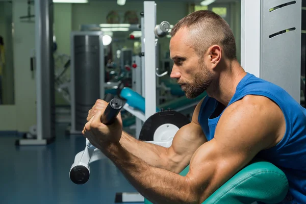 O atleta faz bíceps de bancada no simulador no ginásio. Treinamento muscular da mão no simulador. Músculos tensos de mãos sob carga. Fotos para revistas esportivas, cartazes e sites . — Fotografia de Stock