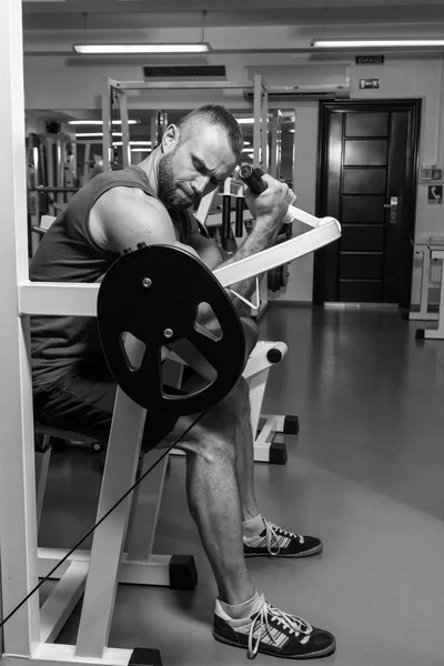 El atleta hace bíceps de banco en el simulador en el gimnasio. Entrenamiento muscular de mano en el simulador. Los músculos tensos de las manos bajo carga. Fotos para revistas deportivas, carteles y sitios web . — Foto de Stock