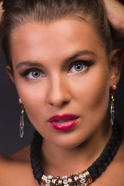 Una hermosa morena con maquillaje elegante y accesorios sobre un fondo oscuro . — Foto de Stock