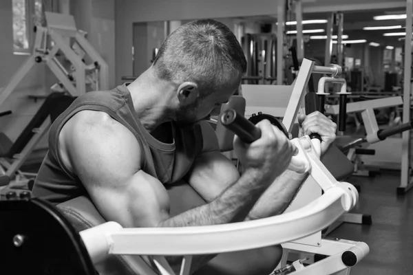 Idrottaren bänk biceps på simulatorn i gymmet. Hand muskelträning på simulatorn. Spända muskler i händerna under belastning. Bilder för idrottsliga tidskrifter, affischer och webbplatser. — Stockfoto