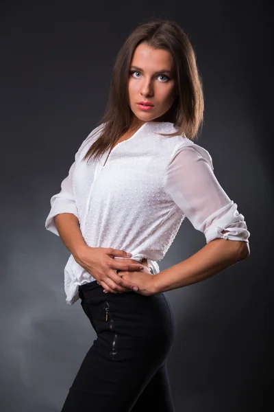 Joven empresaria elegantemente vestida. La imagen de una hermosa joven empresaria. Chica en pantalones negros y una camisa blanca sobre un fondo oscuro. Foto para revistas de moda y sociales, sitios web . — Foto de Stock