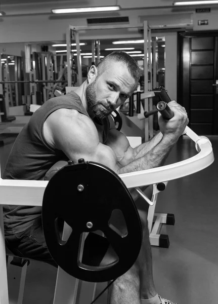 El atleta hace bíceps de banco en el simulador en el gimnasio. Entrenamiento muscular de mano en el simulador. Los músculos tensos de las manos bajo carga. Fotos para revistas deportivas, carteles y sitios web . — Foto de Stock