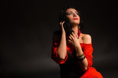 Karanlık bir arka plan üzerinde kırmızı ve siyah elbiseli güzel bir genç kadın portresi.