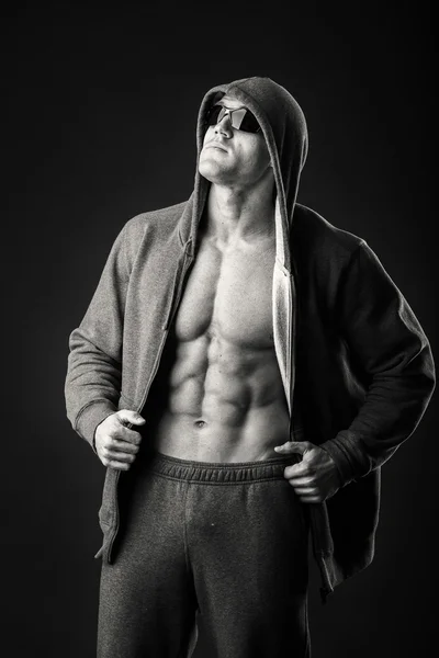 Hombre musculoso con chaqueta deportiva y gafas oscuras sobre fondo negro. Demostración de los músculos del cuerpo durante la chaqueta deportiva. Ropa deportiva y accesorios. Fotos para revistas deportivas y sitios web . — Foto de Stock