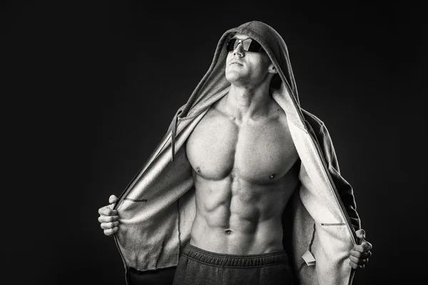 Hombre musculoso con chaqueta deportiva y gafas oscuras sobre fondo negro . — Foto de Stock