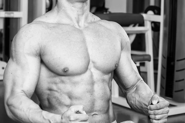 Hombre musculoso fuerte haciendo ejercicios en el gimnasio. Hermoso cuerpo en una foto en blanco y negro. Estilo de vida saludable . — Foto de Stock